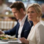 A cinematic medium shot of a married couple sitting at a restaurant table. The man is looking down at his plate, while the woman is looking straight ahead. There's a ring on the table next to the man's hand. The background is blurred.