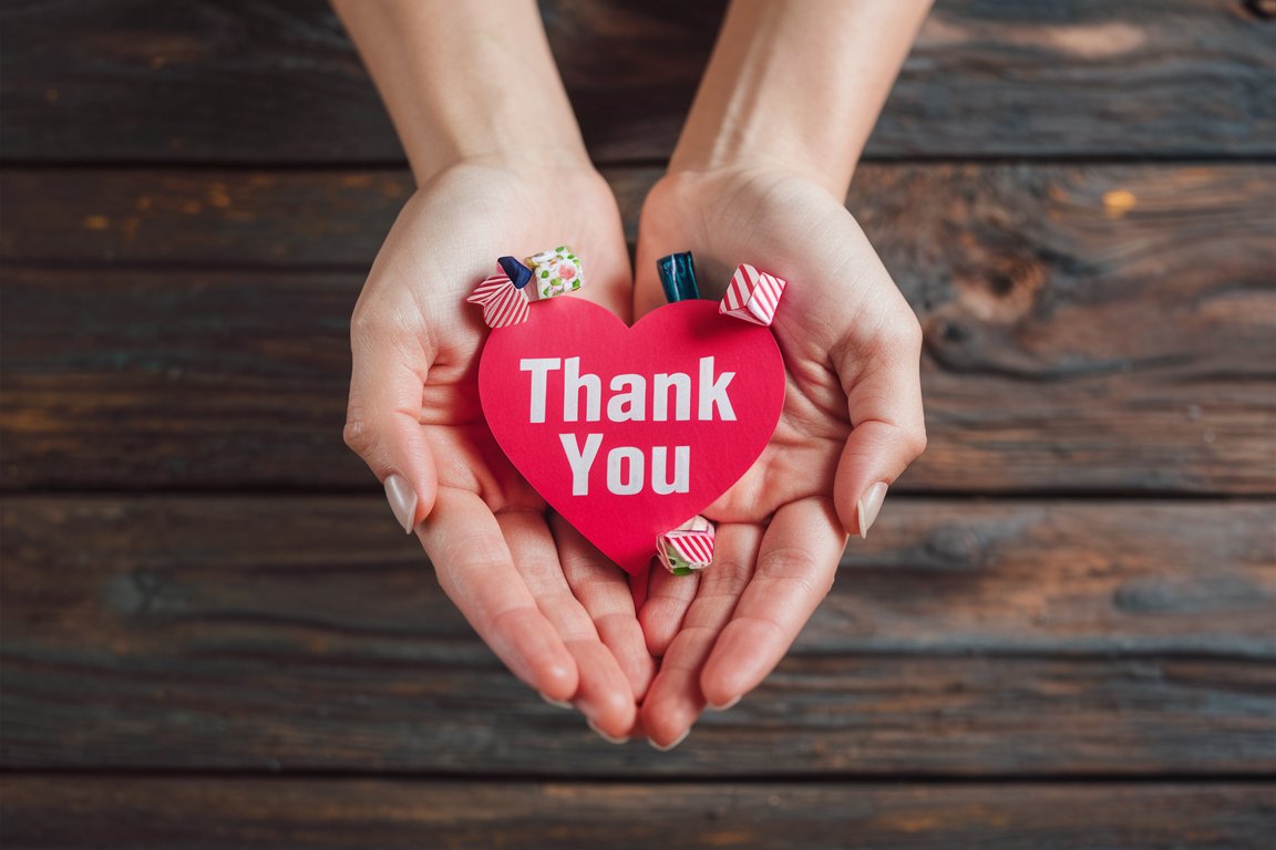 Hands presenting a heart-shaped "thank you" note with small gifts popping out